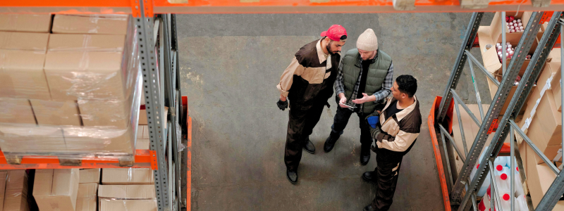 A group of staff in a warehouse discuss energy recommendations on a tablet.